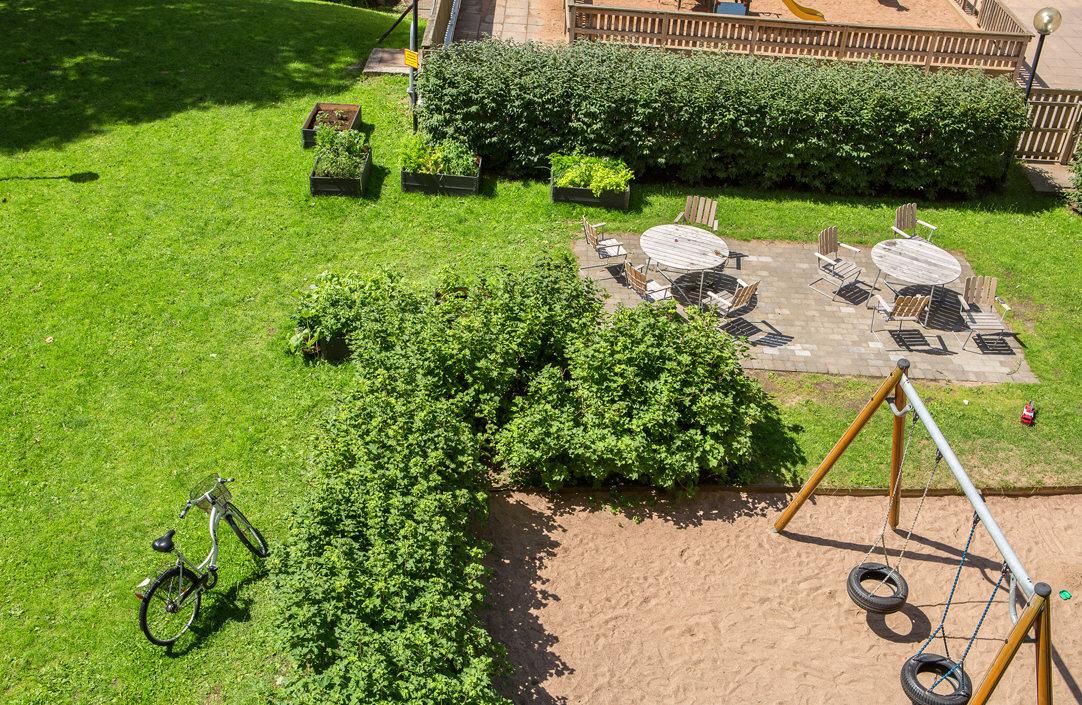 Stor grön innergård med gungor, odlingar och möbler